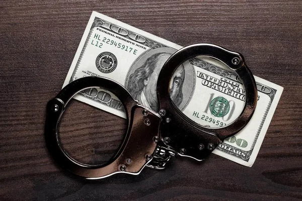handcuffs-and-one-hundred-dollars-on-wooden-table